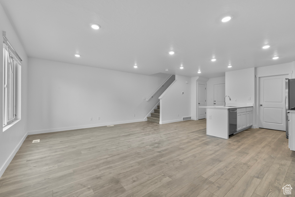 Unfurnished living room with visible vents, a sink, baseboards, stairway, and recessed lighting