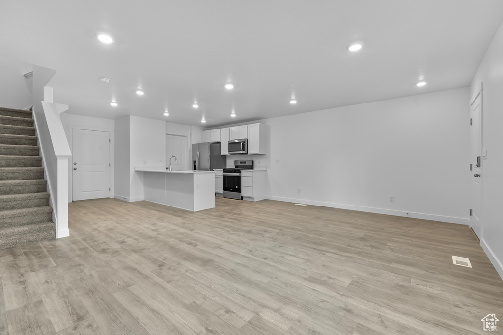 Unfurnished living room with stairway, baseboards, light wood finished floors, and recessed lighting