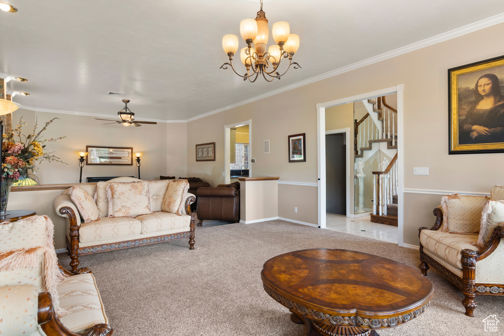 Carpeted living room featuring crown molding, stairs, and ceiling fan with notable chandelier