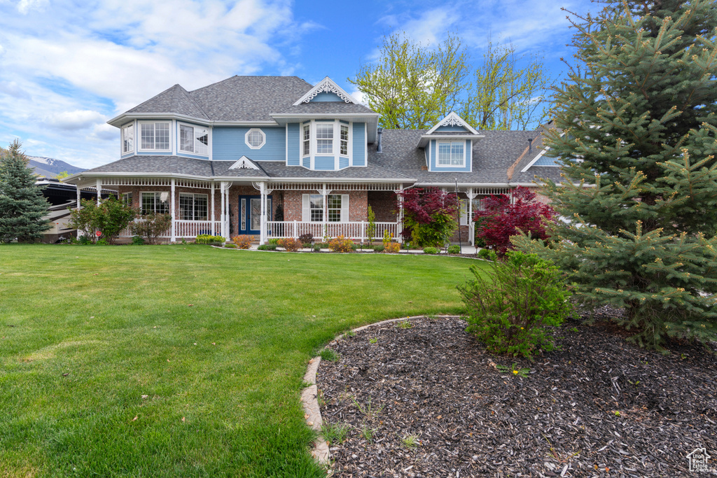Victorian home featuring a porch, a shingled roof, brick siding, and a front yard