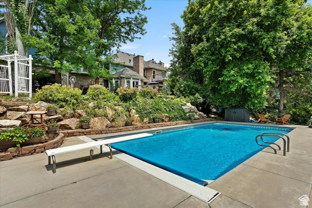 Pool featuring a storage shed, a patio, a diving board, and an outdoor structure
