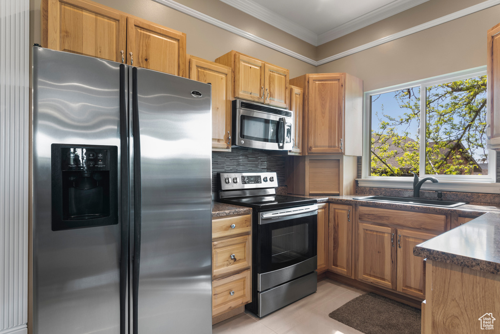 Kitchen with decorative backsplash, crown molding, appliances with stainless steel finishes, dark countertops, and a sink