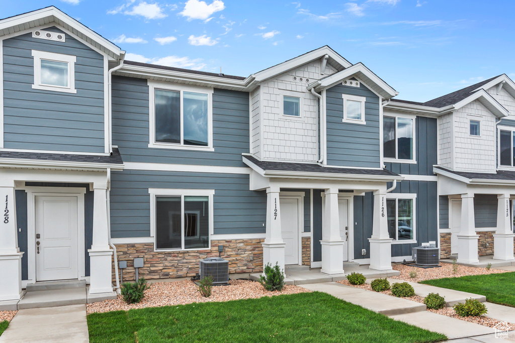 Craftsman-style home featuring central air condition unit, covered porch, a front lawn, and stone siding