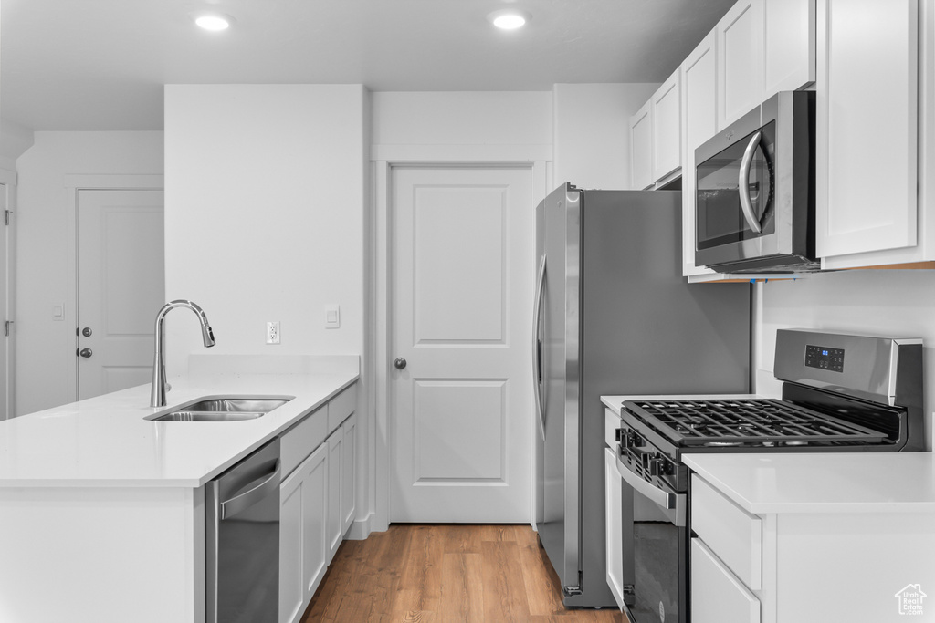 Kitchen with appliances with stainless steel finishes, a sink, a peninsula, white cabinetry, and light wood-type flooring
