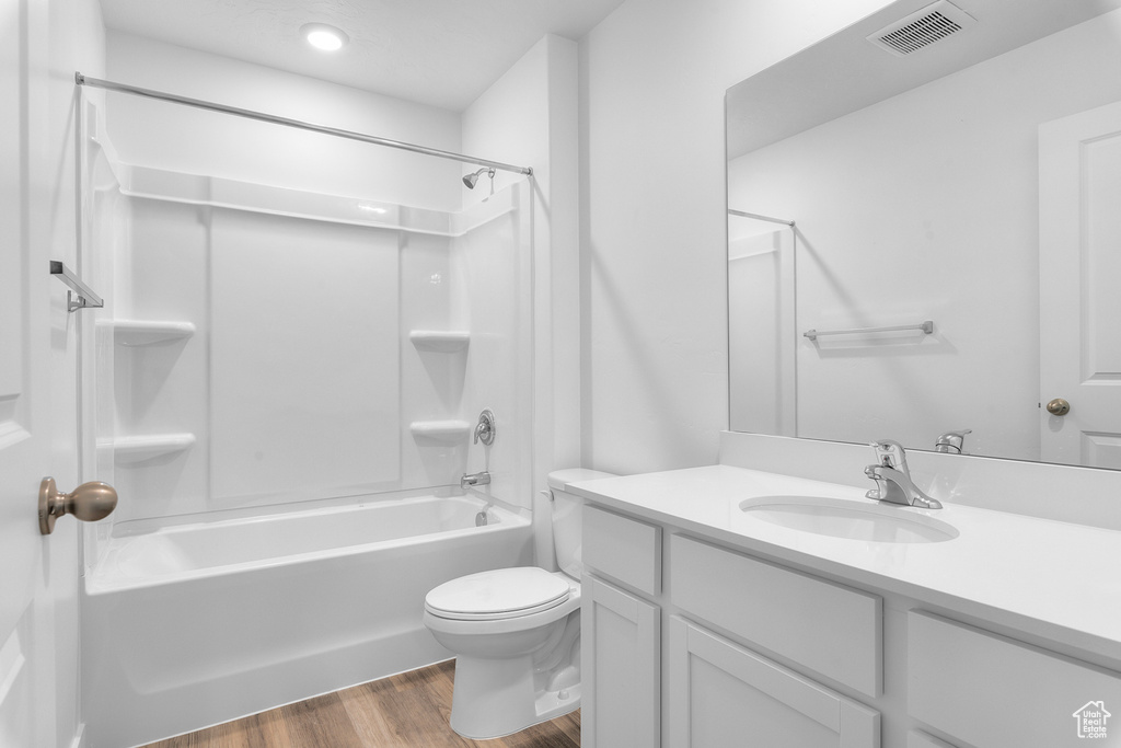 Full bath with vanity, toilet, wood finished floors,  shower combination, and visible vents
