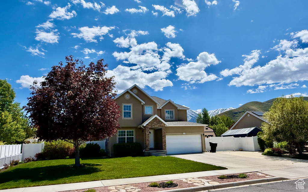 Traditional-style home with fence, a mountain view, concrete driveway, stone siding, and stucco siding