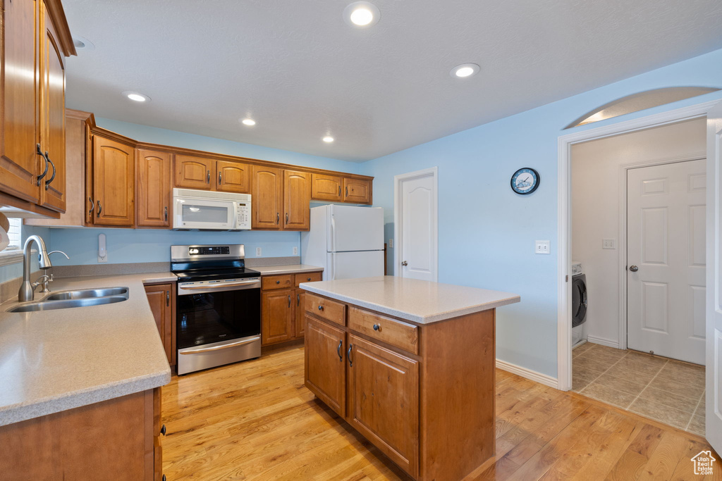 Kitchen featuring white appliances, washer / clothes dryer, light countertops, brown cabinets, and a sink
