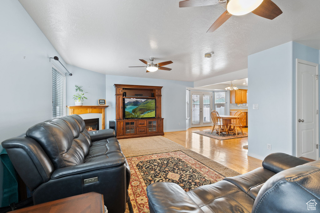Living room with baseboards, light wood finished floors, ceiling fan with notable chandelier, and a warm lit fireplace
