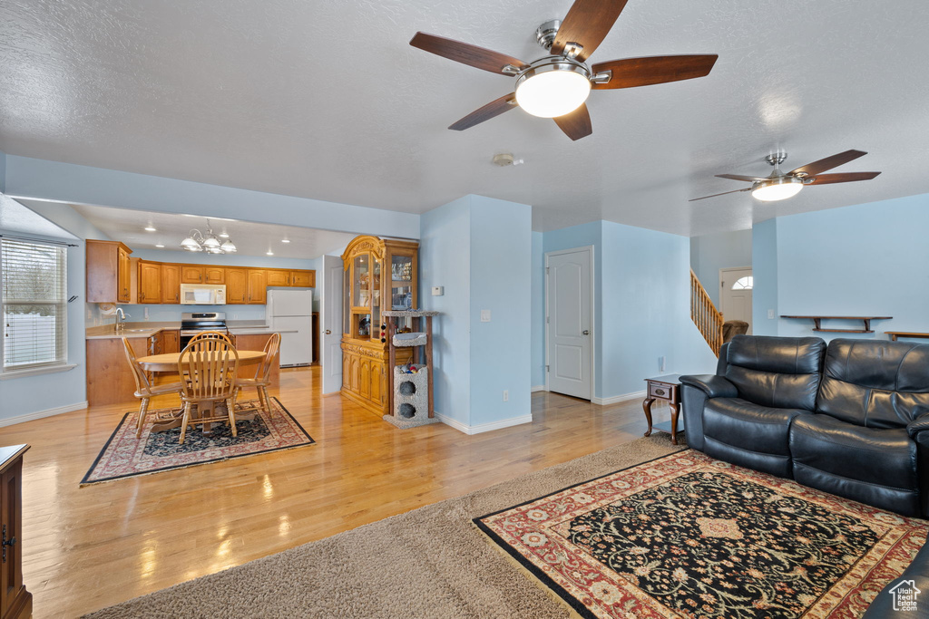 Living room featuring baseboards, light wood-style flooring, and ceiling fan with notable chandelier