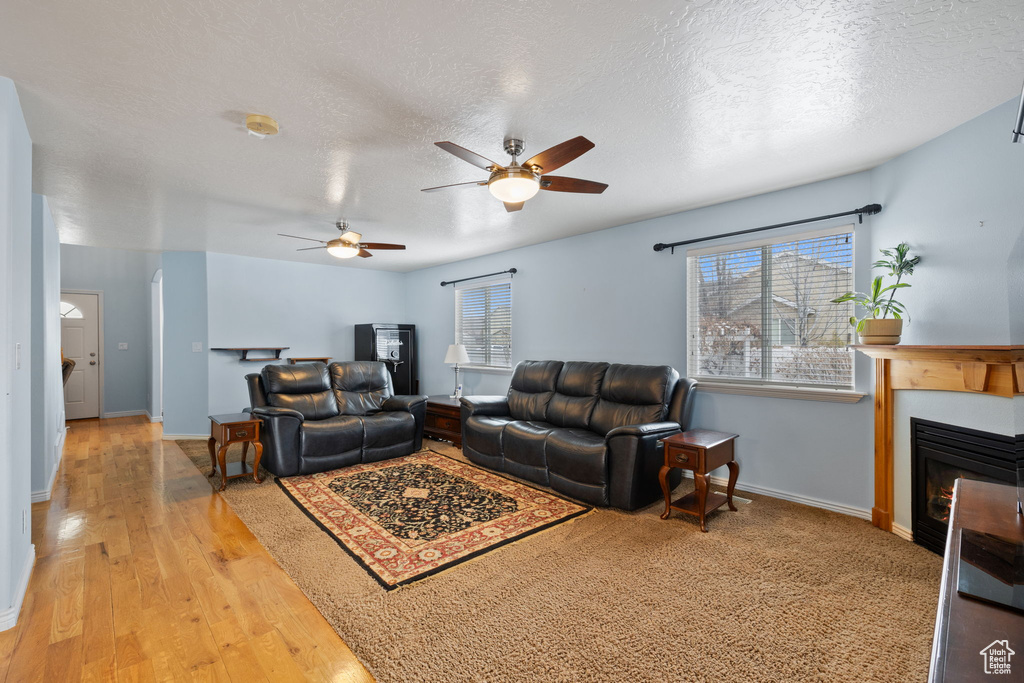 Living room with a textured ceiling, ceiling fan, a glass covered fireplace, and baseboards