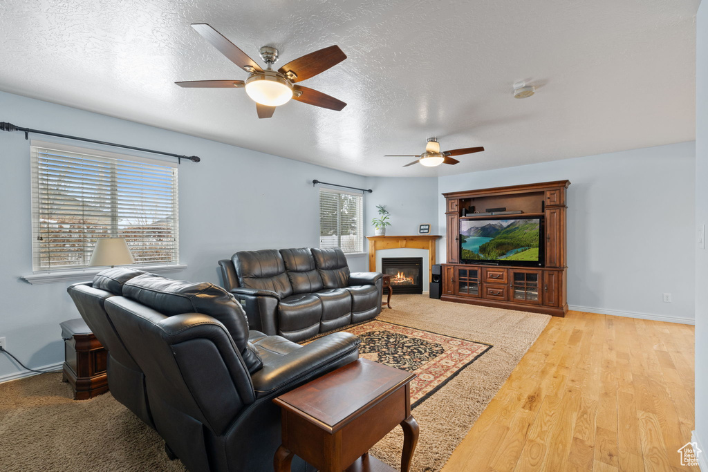 Living room with a glass covered fireplace, baseboards, a ceiling fan, and a textured ceiling