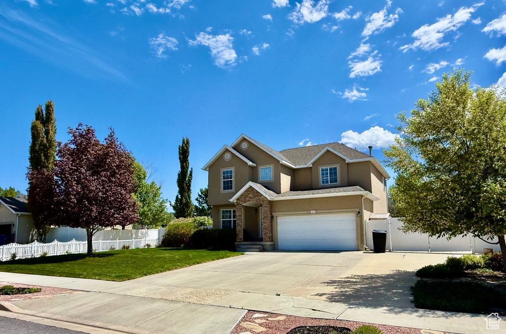 Traditional-style home with concrete driveway, a garage, fence, and stucco siding