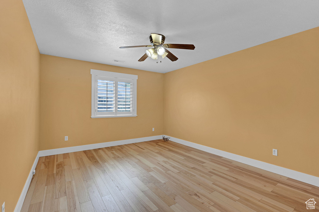Unfurnished room featuring light wood-type flooring, a textured ceiling, baseboards, and ceiling fan