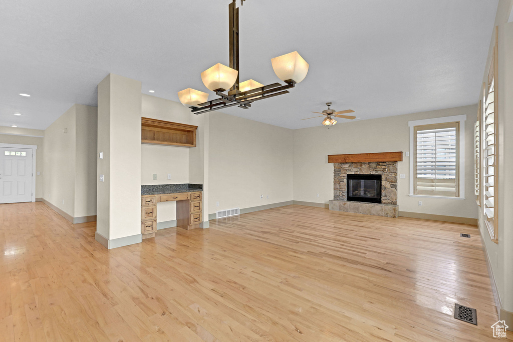 Unfurnished living room with light wood-style floors, ceiling fan with notable chandelier, and visible vents