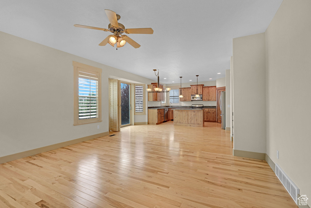 Unfurnished living room with light wood-style flooring, ceiling fan with notable chandelier, recessed lighting, baseboards, and visible vents