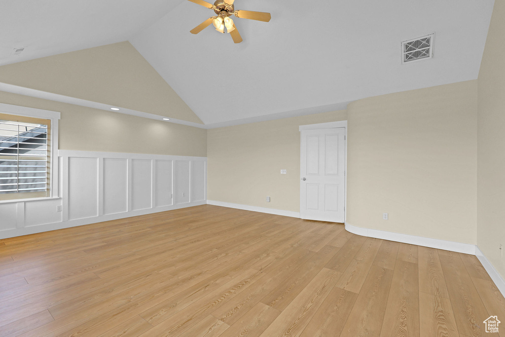 Empty room featuring ceiling fan, wainscoting, high vaulted ceiling, light wood-style flooring, and visible vents