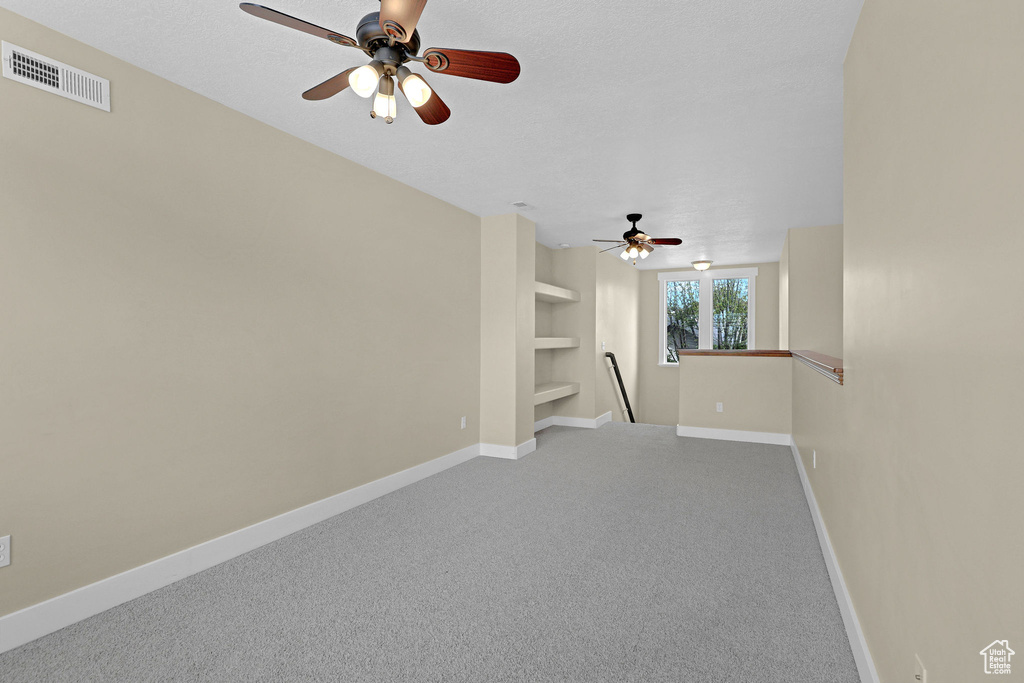 Carpeted spare room with baseboards, ceiling fan, built in shelves, and visible vents