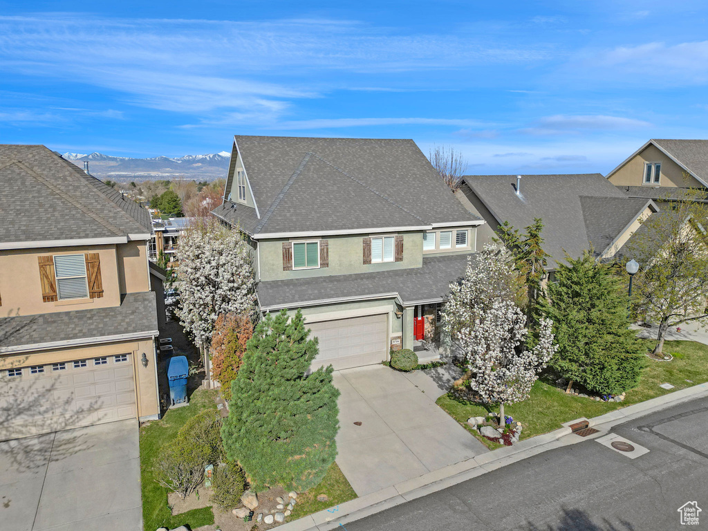 View of front of home with a mountain view, concrete driveway, an attached garage, a shingled roof, and stucco siding