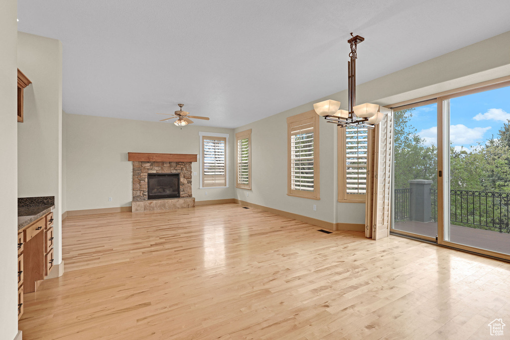 Unfurnished living room featuring baseboards, ceiling fan with notable chandelier, light wood finished floors, and a stone fireplace