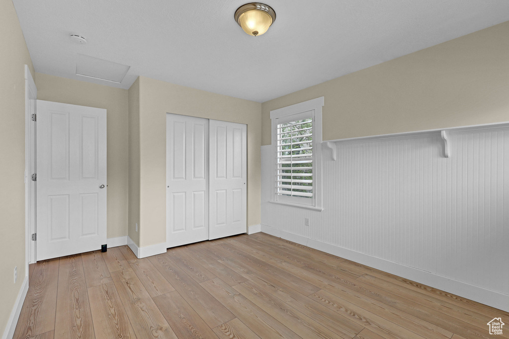 Unfurnished bedroom featuring attic access, wainscoting, light wood-type flooring, baseboards, and a closet