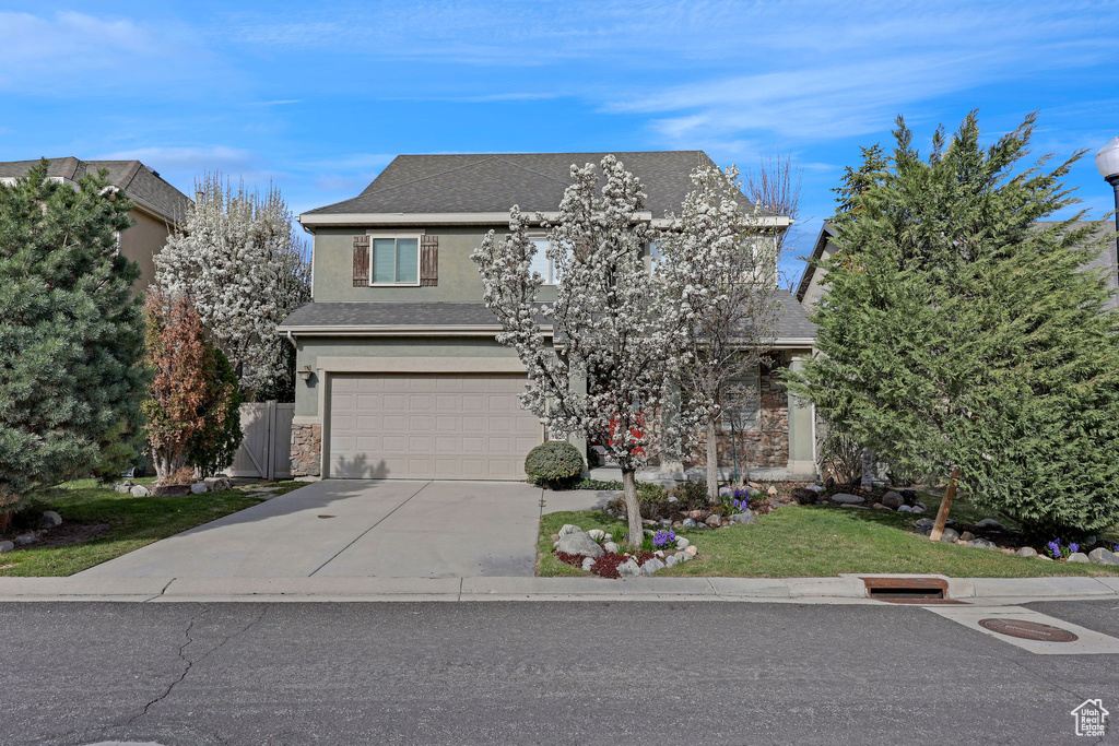 Traditional-style home with a garage, stone siding, roof with shingles, stucco siding, and concrete driveway