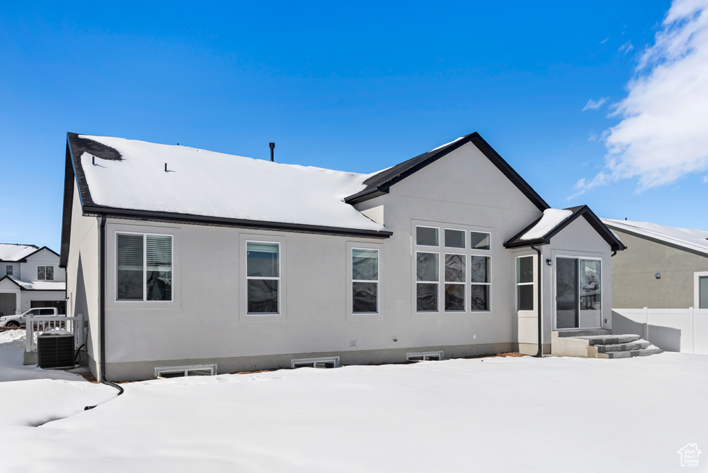 Snow covered rear of property with fence, central AC unit, and stucco siding
