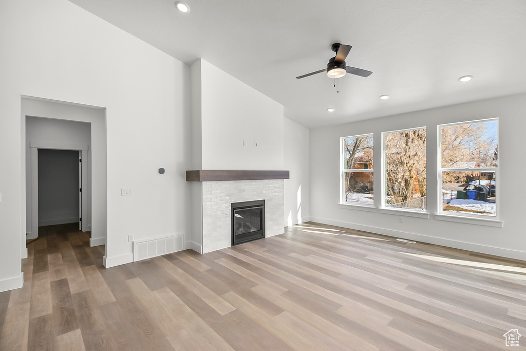 Unfurnished living room featuring a ceiling fan, visible vents, wood finished floors, baseboards, and a glass covered fireplace
