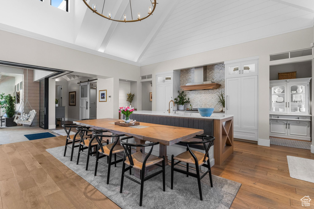 Dining area featuring high vaulted ceiling, light wood-style flooring, a barn door, and a notable chandelier