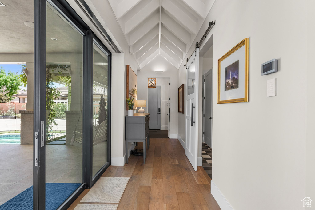 Hall with baseboards, a barn door, vaulted ceiling, and hardwood / wood-style flooring
