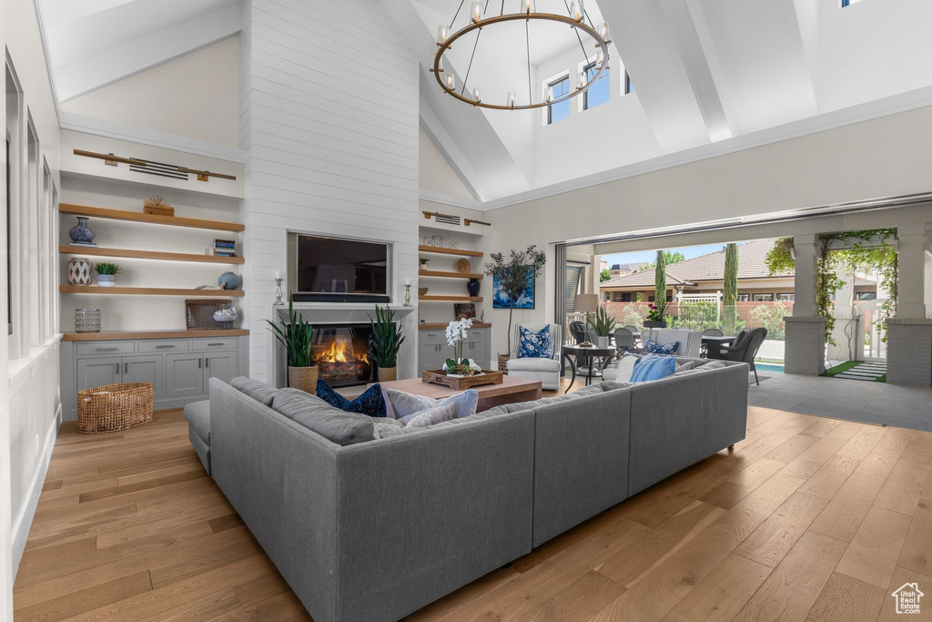 Living room with a glass covered fireplace, high vaulted ceiling, light wood-style floors, and a chandelier