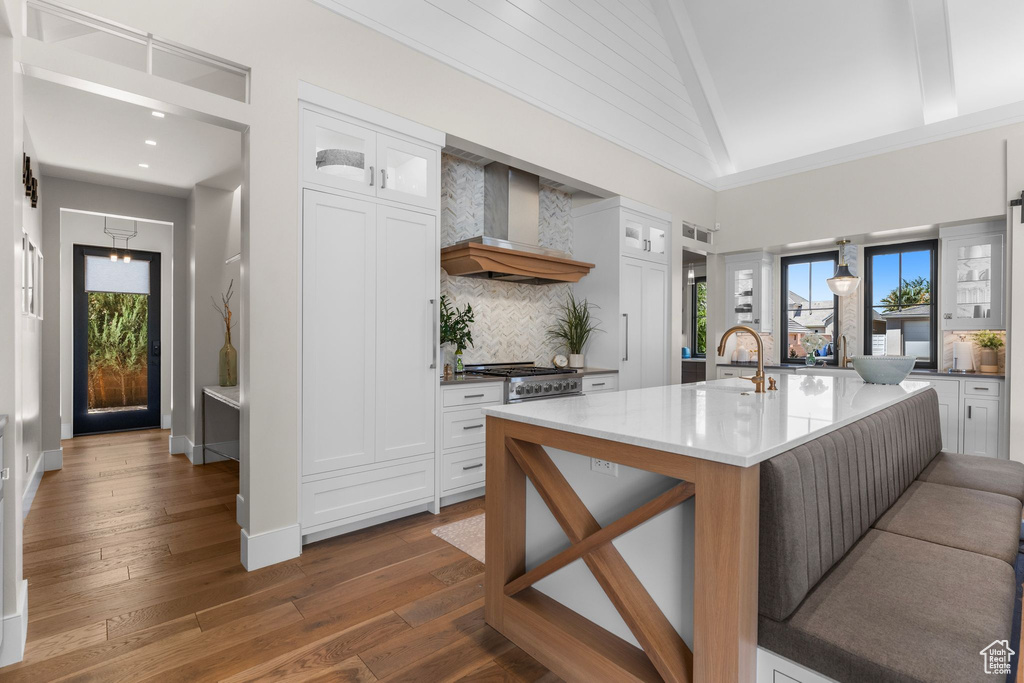 Kitchen with backsplash, white cabinets, a healthy amount of sunlight, and wall chimney exhaust hood