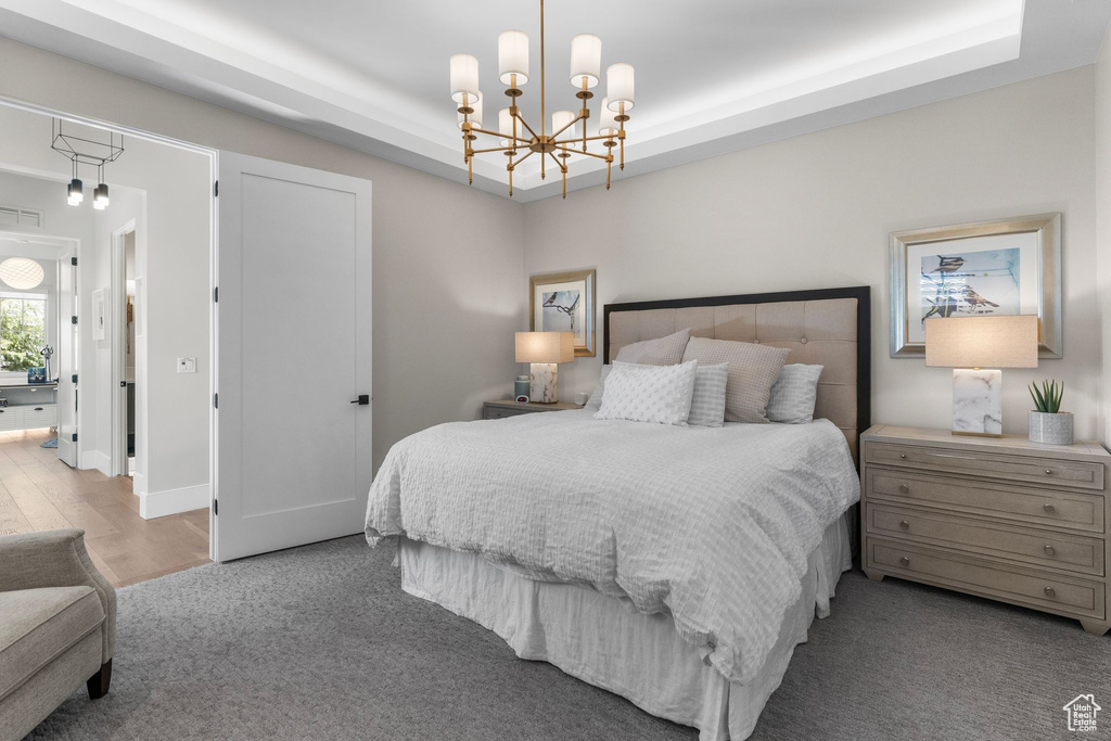 Bedroom with a raised ceiling, wood finished floors, and a chandelier