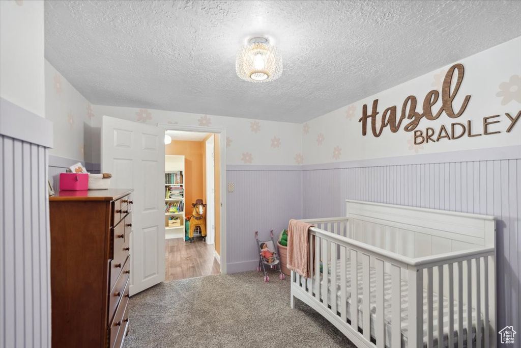 Bedroom featuring a nursery area, carpet floors, wainscoting, and a textured ceiling