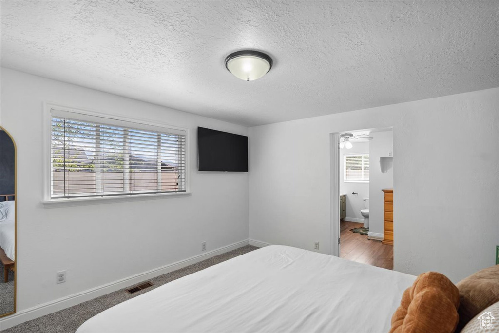 Bedroom featuring baseboards, ensuite bath, a textured ceiling, and visible vents