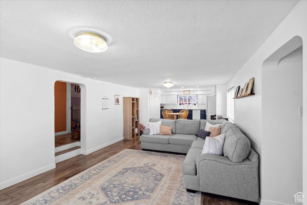 Living area with arched walkways, baseboards, a textured ceiling, and wood finished floors