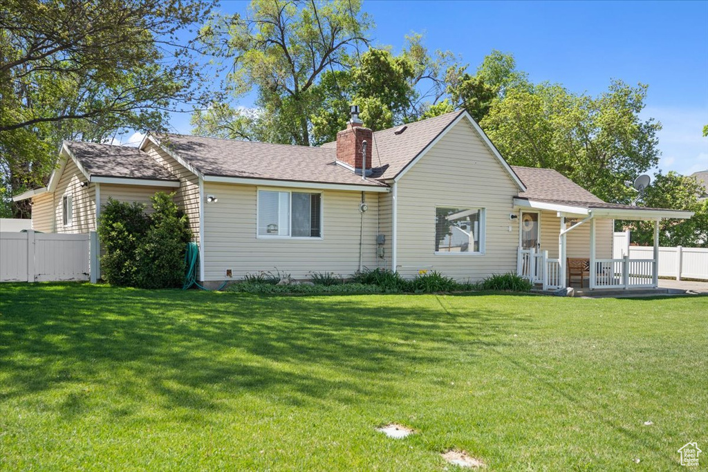 Rear view of house featuring a lawn, fence, a chimney, and roof with shingles