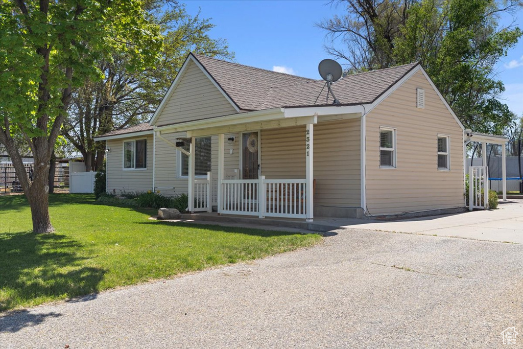 View of front of house featuring a porch, a front lawn, roof with shingles, and driveway