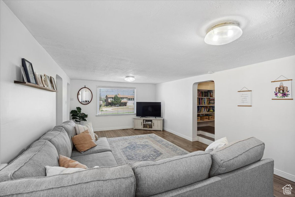 Living area with arched walkways, baseboards, a textured ceiling, and wood finished floors