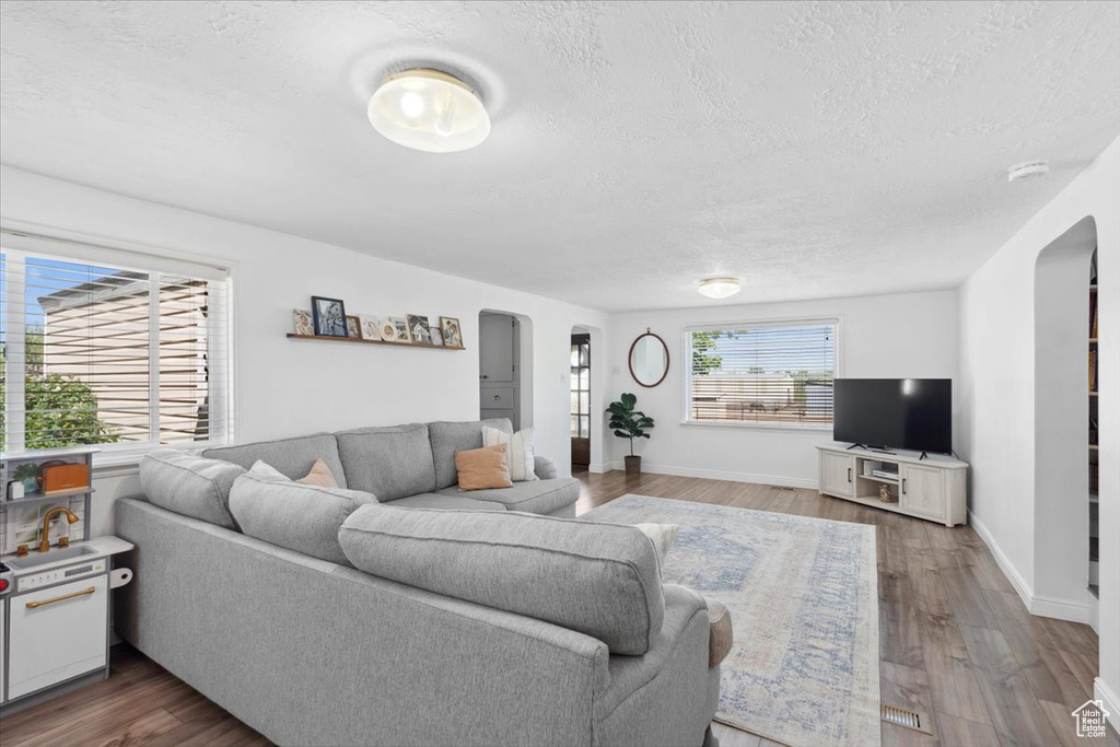 Living area featuring baseboards, arched walkways, a textured ceiling, and wood finished floors