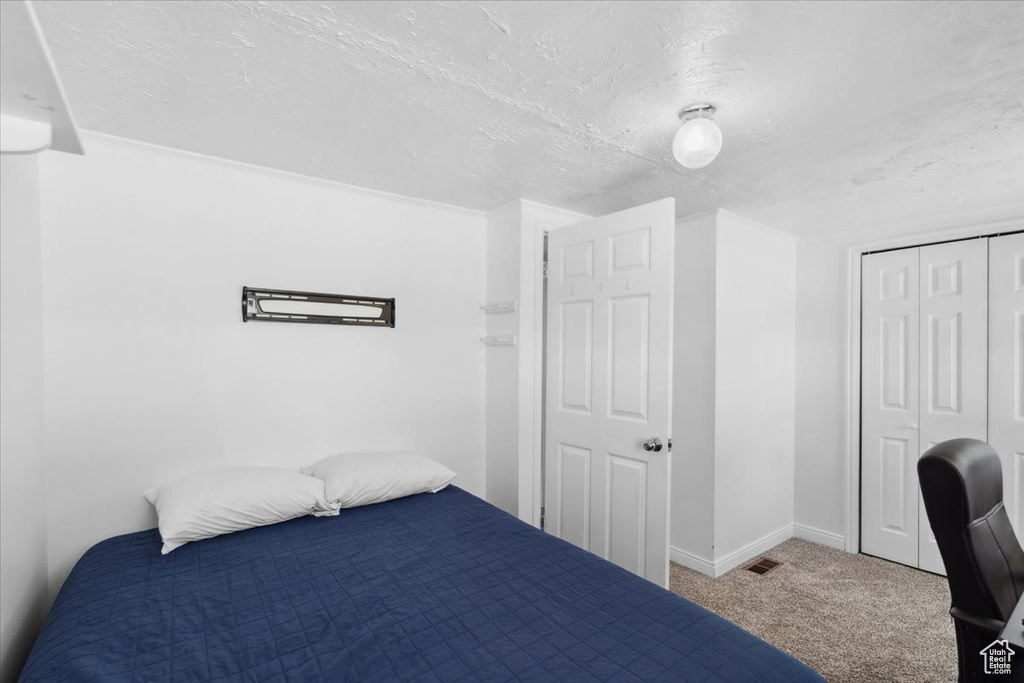 Bedroom with a textured ceiling, visible vents, baseboards, a closet, and carpet