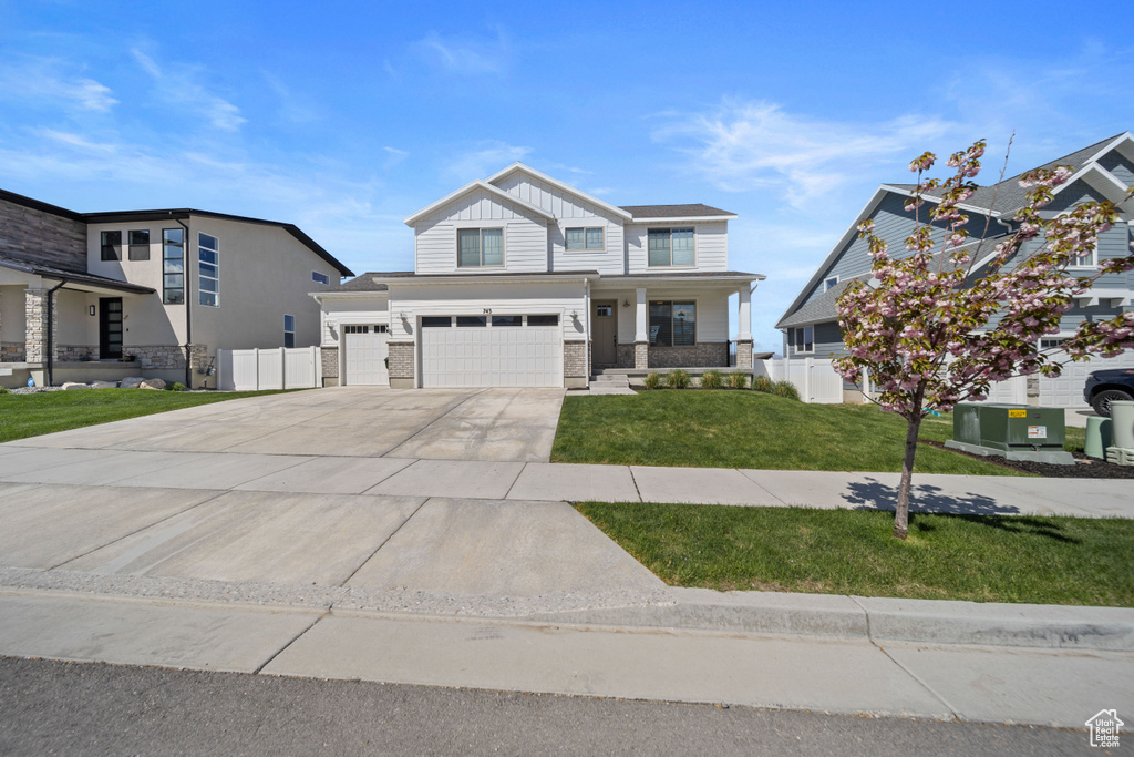 View of front facade with driveway, a front yard, fence, an attached garage, and stone siding
