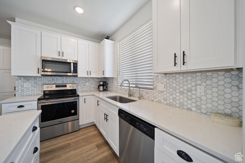 Kitchen featuring backsplash, light stone countertops, a sink, stainless steel appliances, and white cabinetry