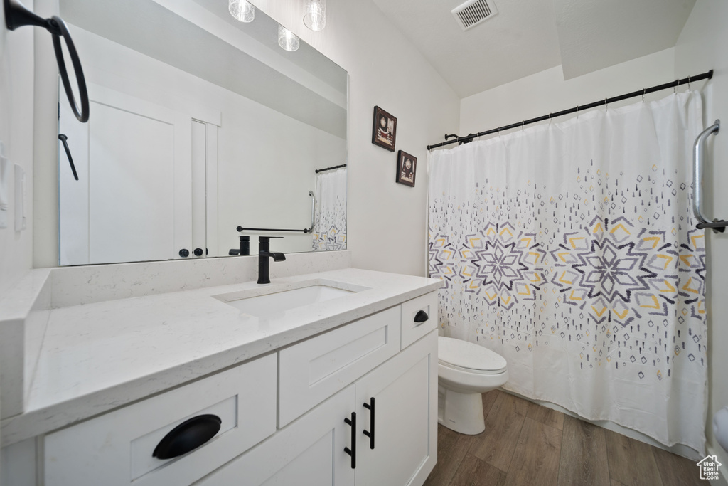 Full bathroom with vanity, toilet, a shower with shower curtain, wood finished floors, and visible vents
