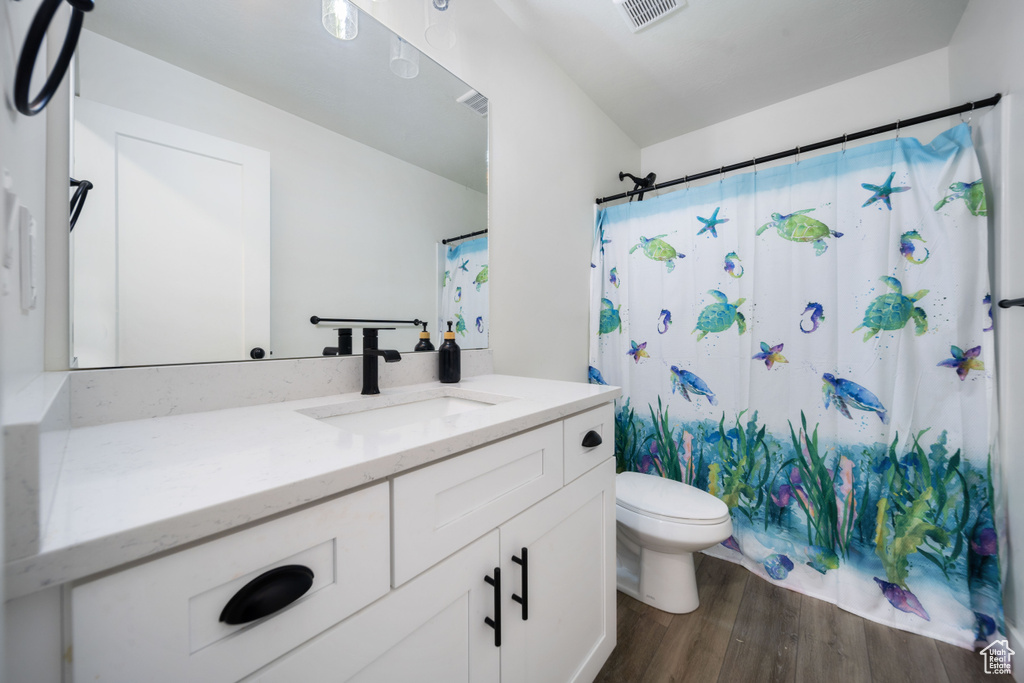 Bathroom featuring visible vents, curtained shower, wood finished floors, vanity, and toilet