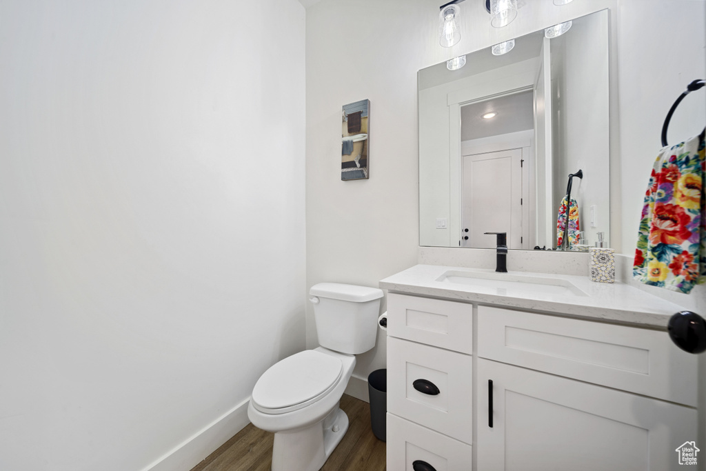 Half bathroom with vanity, baseboards, toilet, and wood finished floors
