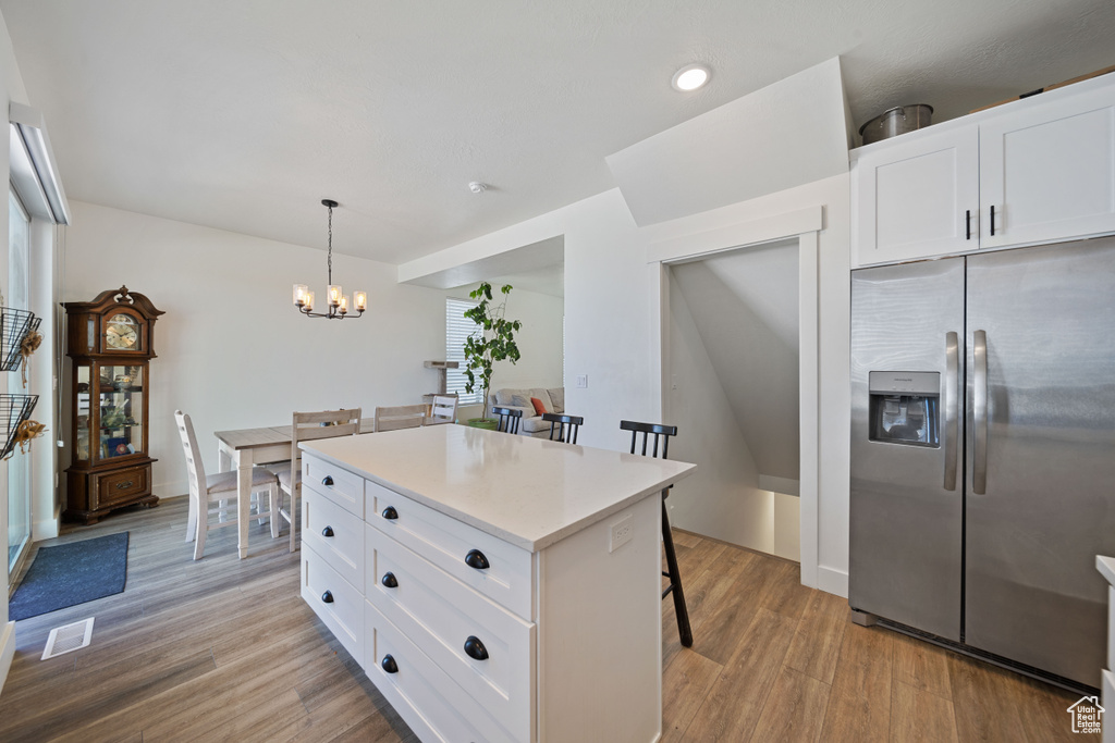 Kitchen with a kitchen breakfast bar, visible vents, stainless steel fridge with ice dispenser, an inviting chandelier, and light wood-style flooring