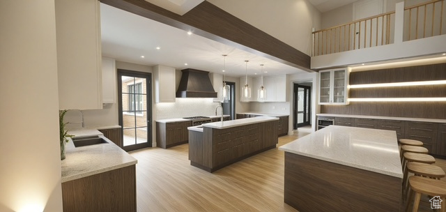 Kitchen with a kitchen island with sink, light wood-type flooring, recessed lighting, wall chimney exhaust hood, and a sink