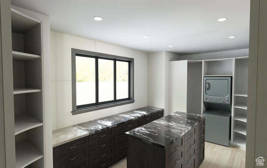 Kitchen with open shelves, stacked washing maching and dryer, recessed lighting, stone counters, and light wood finished floors