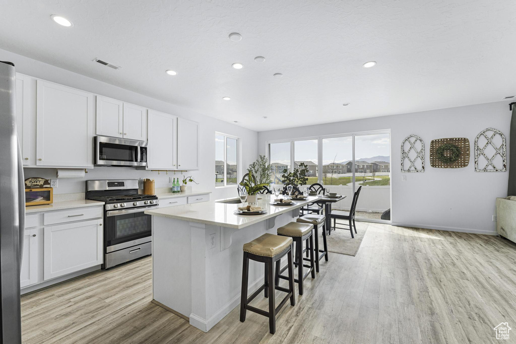 Kitchen with a kitchen bar, a center island, light wood finished floors, stainless steel appliances, and recessed lighting