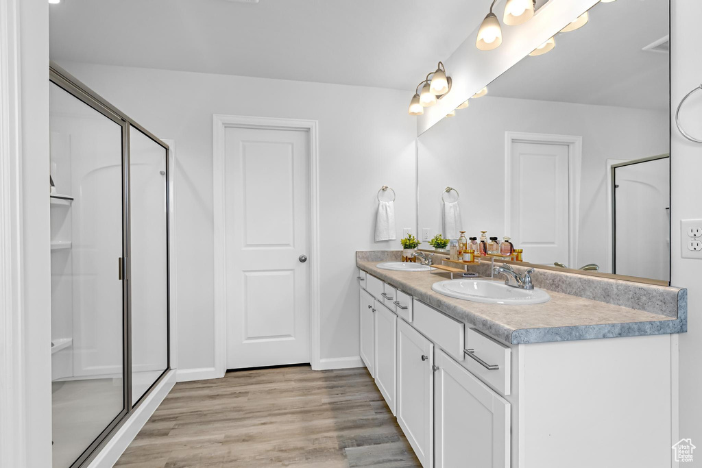 Bathroom with double vanity, a stall shower, a sink, and wood finished floors
